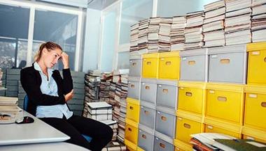 Stressed woman at work looking at full file cabinets